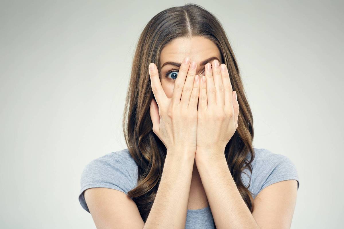 Junge Frau mit ängstlichem Blick hält sich die Hände vors Gesicht – Symbolbild für Angstüberwindung